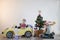 Funny little smiling kids driving toy car with Christmas tree. Happy child in colour fashion clothes bringing hewed xmas tree from