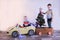 Funny little smiling kids driving toy car with Christmas tree. Happy child in colour fashion clothes bringing hewed xmas tree from