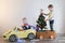 Funny little smiling kids driving toy car with Christmas tree. Happy child in colour fashion clothes bringing hewed xmas tree from