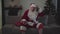 Funny male Caucasian Santa Claus sitting on sofa and watching sports game on TV. Senior joyful fan resting at home after