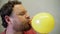 Funny man with a beard and mustache inflates a yellow balloon with his mouth