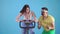 Funny man coach of 80`s with mustache trains a young woman on exercise bike on a blue background