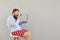 Funny man in red shorts with a laptop increases magnifying information on a gray background. Concept of online