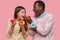 Funny mixed race young woman and man taste delicious donuts, like sweet dessert, bite pastry, stand closely, isolated