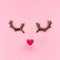 Funny muzzle made of red heart and wooden reindeer horns on a pink background