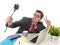 Funny nerd businessman at office desk taking selfie photo with mobile phone camera and stick