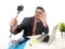 Funny nerd businessman at office desk taking selfie photo with mobile phone camera and stick