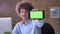 Funny nerdy businessman with volume curly hair pointing phone with chroma key into camera, sitting and working in modern