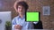 Funny nerdy office worker with volume curly hair pointing tablet with chroma key at camera and smiling, man with