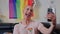 Funny non-binary European influencer person takes a selfie in front of a rainbow pride flag.