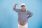 Funny obese sailor man with captain hat shows muscles on arm on light blue background