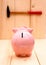 Funny pink piggy bank in focus and hammer on wood