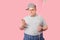 Funny plump guy standing with phone and balloons having doubts isoated on pink