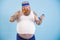 Funny plus size man eats chicken leg and does exercises with dumbbell on blue background