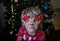 Funny portrait of cute boy 5 years old in a festive make-up of a deer in front of the Christmas tree