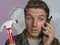 Funny portrait of messy and frustrated man calling domestic insurance on mobile phone for repair mess he did with a hammer