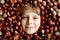 Funny portrait of preteen or school kid boy with lots of chestnuts. Smiling happy child having fun on autumn day with a