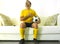 Funny portrait of young man in football team uniform watching soccer game on TV at home couch listening national anthem with hand