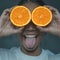 Funny portrait of young woman showing tongue out while covering her eyes with halves of orange