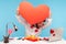 Funny positive bearded man peeping out big red paper heart he holding, preparing greeting card, sitting at workplace all covered