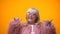 Funny positive elderly female in pink coat making rocker gesture, having fun