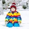 Funny preschool boy in colorful clothes happy about snow, outdoors