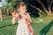 Funny preschool Caucasian child girl blowing soap bubbles in park at summer sunset