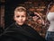 Funny preschooler boy getting haircut. Children hairdresser with the trimmer is cutting little boy in the room with loft