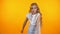 Funny preteen girl dancing, moving to music isolated on orange background