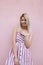 Funny pretty young blond woman in a pink fashionable striped sundress with a positive smile poses near the vintage pink wall