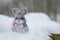 Funny rabbit in snow, christmas or easter concept. A toy gray hare sits in a snowdrift against the backdrop of a forest