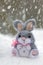 Funny rabbit in snow, christmas or easter concept. A toy gray hare sits in a snowdrift against the backdrop of a forest