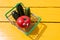 Funny red tomato with eyes and green cucumbers in the small supermarket basket on the yellow background. Vegetarian concept