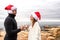 Funny romance scene of a beautiful happy young couple celebrating Christmas standing outdoor face to face wearing Santa Claus hat