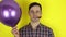 A funny, sad guy with a purple balloon in his hand blows in a party horn showing that he is not having fun at the party.