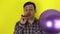 A funny, sad guy with a purple balloon in his hand blows in a party horn showing that he is not having fun at the party.