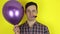 A funny, sad guy with a purple balloon in his hand blows in a party horn showing that he is not having fun at the party.