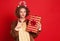 Funny sad unsatisfied woman in a Christmas reindeer costume  with unsuccessful gift on colorful red background