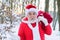 Funny Santa Claus coming to the winter forest with a bag of gifts, snow landscape.