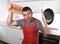 Funny scared man holding pan wearing apron at kitchen asking for help