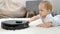 Funny shot of curious little baby boy exploring and looking at working robot vacuum cleaner