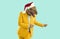 Funny showman in yellow suit, Santa hat and rubber dinosaur mask dancing on turquoise background.