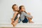 Funny siblings sitting on a table with their legs up. Over white wall