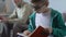 Funny small kid in glasses reading book with happy grandfather behind, bookworm