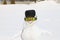 A funny smiling white snowman in a black cap, glasses and headphones stands in a snowy meadow in winter, on Christmas and New Year
