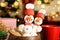 Funny snowmen made of marshmallows in wooden bowl against blurred festive lights, closeup