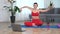 Funny sportive smiling woman sitting on yoga mat makes wave with hands at home