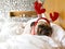 Funny tired pug dog laying on her side sleeping rest while wearing Christmas reindeer antlers on bed, wrap with blanket and