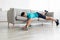 Funny tired young caucasian male lies on sofa with dumbbell in living room interior, rest after training