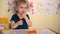 Funny toddler girl child eating carrots sitting by table in her room